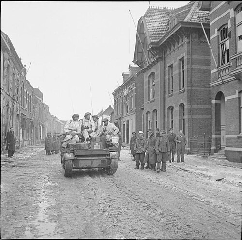 Snow-suited troops of 131st Brigade, 7th Armoured Division, in Universal Carriers drive past German POWs in Echt, 18 January 1945.