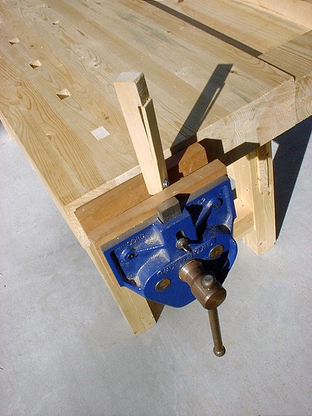 A woodworker's face vise with its dog extended, holding (without using the dog) a wooden bench dog being worked