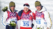 Drie skiërs poseren voor de fotografen, de een in het midden houdt de andere twee bij de armen vast.