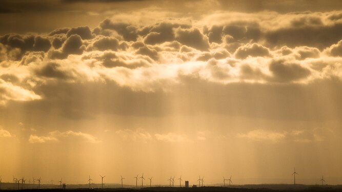 Old winding tower among green energy wind turbines