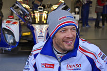 Photo d'un homme souriant, portant un bonnet gris et une combinaison de course