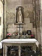 Autel blanc surmonté d'une croix et de pots de fleurs. Au-dessus, dans une niche, statue blanche de femme tenant un crucifix avec, à ses pieds, un bouquet de roses.