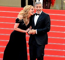 A photograph of Julia Roberts and George Clooney laughing at the 2016 Cannes Film Festival