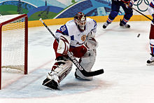 Ilya Bryzgalov ist auf dem Eis und lenkt einen Hockey-Puck ab. Er trägt ein weiß-blaues Trikot mit roten Hosen.