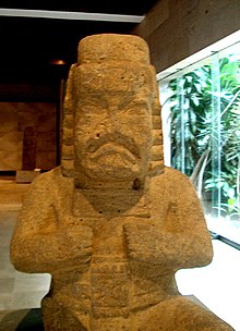 A stone Olmec werejaguar, showing common werejaguar characteristics including a downturned mouth, almond-shaped eyes, pleated ear bars,
a headdress with headband, and a crossed-bars icon on the chest Jaguarbaby.jpg