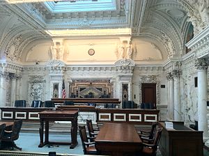 An ornate courtroom with marble columns, eleven chairs in two rows for judges, and an old fashioned wooden lectern.