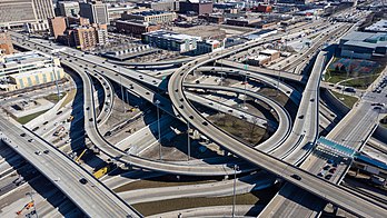 Vista aérea do Jane M. Byrne Interchange, um trevo rodoviário perto do centro de Chicago, Illinois, Estados Unidos. É a junção entre as vias expressas Dan Ryan, Kennedy e Eisenhower, e a rua Ida B. Wells Drive. O nome oficial deste trevo refere-se a Jane Byrne, a primeira prefeita de Chicago. Desenvolvido no final da década de 1950 e na década de 1960, o trevo em sua configuração original tornou-se notório por congestionamentos. Em 2004, foi classificado como o terceiro pior gargalo de tráfego do país, com aproximadamente 400 mil veículos por dia que o utilizam perdendo um total de 25 milhões de horas a cada ano. Isso levou a uma reconfiguração de 800 milhões de dólares, que começou em 2013 e ainda está em andamento. (definição 4 000 × 2 250)