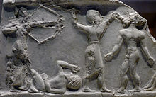 Photographie d'un bas-relief. On y reconnaît quatre personnages : à gauche un archer debout à l'arc bandé, à ses pieds un homme couché à terre, au centre un homme debout qui tient d'une main le quatrième (également debout) par la tête et s'apprête à lui porter le coup fatal de l'autre main.