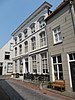 Groot huis met gebosseerd gepleisterde gevel, segmentvormig overtoogde vensters, schilddak