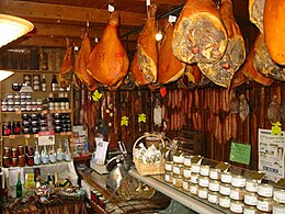 interiér francouzského obchodu s potravinami, s klobásami a šunkami visícími na stropních hácích a sklenicemi produktů z uzenin na policích