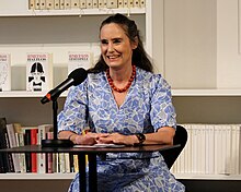 Tanja Kinkel während einer Lesung an Tisch mit Mikro sitzend, ins Publikum lächelnd