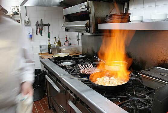 Chef is flambéing pork meat in a restaurant kitchen.