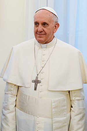 Pope Francis in ordinary dress (white cassock with matching pellegrina and with white fringed fascia, pectoral cross, and white zucchetto).