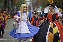 Deux femmes en costumes des personnages Alice et la Reine de Cœur, soit une robe bleue et un tablier blanc à gauche, et une robe rouge et noire à droite.