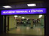 The dark interior of a building with a rectangular, blue sign reading "HEATHROW TERMINAL 4 STATION" in white letters and white flooring