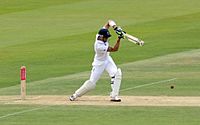 Ein Mann, der einen Helm und weiße Kleidung trägt, während er einen Cricketschläger schwingt.