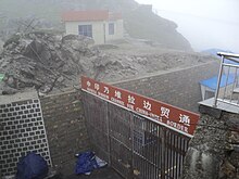 Un pasaje amurallado cerrado por una puerta de metal coronada por una doble inscripción en chino e inglés.