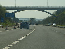 multi-carriageway road with vehicles passing under an elevated roadway. And distant view of sea beyond