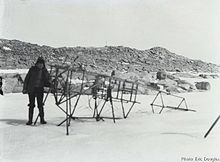 Photo en noir et blanc d'un squelette métallique d'avion posé sur la neige, une personne postant devant.