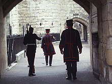 A Yeoman Warder (centre) is escorted by a sentry (left) of the Tower of London Guard. Entrance to 'Tower of London'.jpg