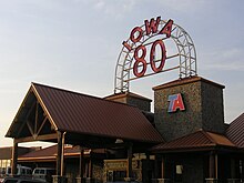 Un grande edificio con una linea del tetto a punta alta.  Una grande insegna al neon recita "Iowa 80".