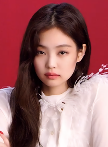 Jennie faces forward in a white blouse against a red backdrop