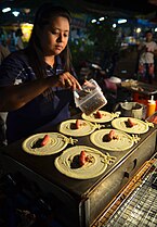 Thai khanom Tokiao being prepared, a Thai style crêpe with a hot dog sausage, at a night market