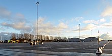 Large free concrete area on which long rectangular fields are marked with white paint in the block.  In the background you can see industrial buildings and tall lamps.