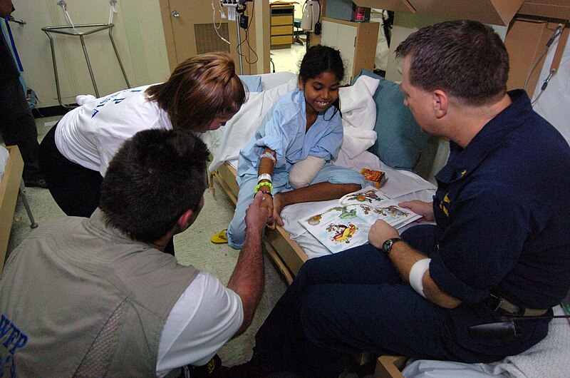 File:US Navy 050212-N-8629M-048 New York Giants quarterback Kurt Warner, center, and his wife Brenda Sue visit a 15-year old Indonesian amputee patient who is learning to read her first English words.jpg
