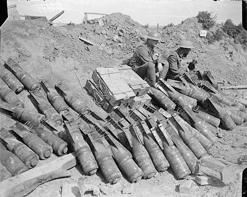 1918, near Lens in France. Two men of the 9th Battalion, Royal Sussex Regiment sit beside a dump of trench mortar bombs.