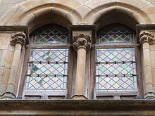 Fotografía en color de una ventana doble de piedra con un arco gótico enmarcado por pequeñas columnas.  La bahía está equipada con vidrieras en forma de diamante.