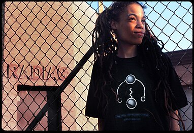 Hafsa Brahim, an artist living near the Brooklyn waterfront, is wearing a "Distressed Human" T-shirt in front of her neighbor, Radiac in 1994. The radioactive waste management company carried radioactive waste through the residential areas of Williamsburg. Hafsa Brahim in front of Radiac, Williamsburg, Brooklyn, 1994.jpg