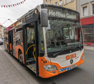 Das Foto zeigt einen Bus, der gerade ohne Fahrer oder Fahrerin ist und auf der Anzeige „HofBus GmbH“ hat. Es zeigt die Zugehörigkeit zum Unternehmen.