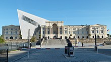 Barevná fotografie s pohledem na historizující budovu muzea, ze které ční moderní architektonický prvek v podobě lichoběžníku