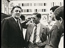 Quatre hommes, dont un avec des lunettes, sur un parking - sur la gauche, on reconnaît Federico Fellini et Pier Paolo Pasolini