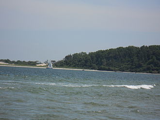 Sailboat beating upwind into the channel in Ipswich Bay. Castle Hill and Crane's Beach are visible in the background. The tide is high. A breaker on Sandy Point is visible in the foreground. Sailboat from Sandy Point.JPG
