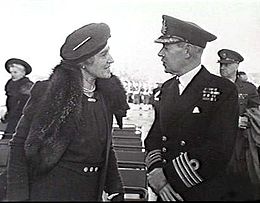Vrouw in donkere jas en hoed in gesprek met man in donker militair uniform