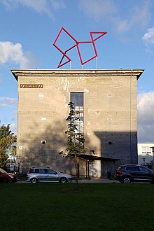 Nella foto si vede la sagoma rettangolare del vecchio rifugio antiaereo chiamato Bunker D con la scultura rossa Cubus Balance al centro del tetto.