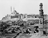 Unha mesquita de varias cúpulas domina a Cidadela amurallada, con tumbas en ruínas e un minarete solitario diante.