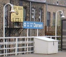 Un panneau rectangulaire bleu indiquant "Damen" au centre entouré d'informations auxiliaires est flanqué de chaque côté de deux luminaires qui dépassent de la balustrade et se courbent vers la plate-forme, offrant la forme dite de "col de cygne".  Les garde-corps et les luminaires sont peints en blanc.