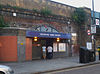 An entrance under a railway brick viaduct with a blue sign reading 