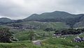 Hiraodai panorama: the Karst Plateau in the center picture, Mount Ohira in foreground, and Hiraodai Branch Path is running through the plateau. It leads to Yogenbaru, in the middle of Mount Ohira, has many limestone pillars lying on the ground. 平尾台パノラマ：中央はカルスト台地で前方に大平山がそびえる。平尾台支線林道が石灰岩柱が連なる羊群原へ向かって走り抜ける。