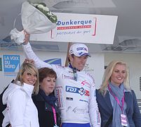 De trois-quarts, quatre personnes sourient. Un coureur cycliste au maillot blanc, lève un bouquet blanc.