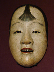 Masque peint en blanc, visage jeune, lèvre rouge et mèche de cheveux sur le font.