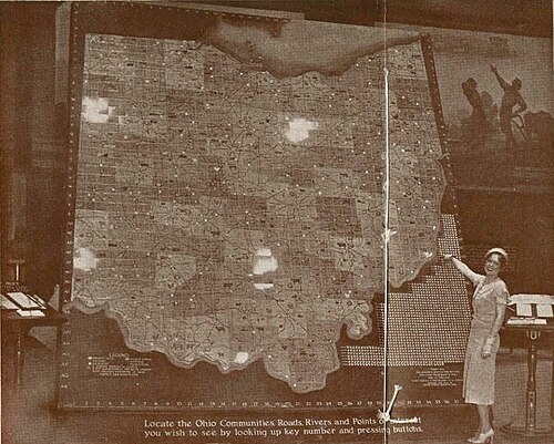 A woman points to an enormous map of Ohio; the caption reads: "Locate the Ohio Communities Roads, Rivers, and Points of Interest you wish to see by looking up key number and pressing buttons."