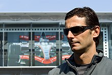 Photo d'un homme avec des lunettes de soleil, devant un garage de course