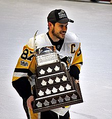 Crosby sur la glace avec une casquette noire et un trophée dans les mains