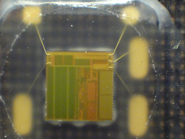 4 by 4 mm silicon chip in a SIM card, which was peeled open. Note the thin gold bonding wires and the regular, rectangular digital-memory areas.