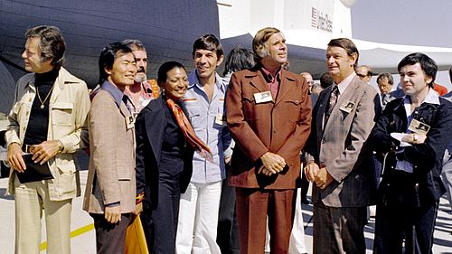 Zleva: DeForest Kelley (Leonard McCoy), George Takei (Hikaru Sulu), James Doohan (Montgomery Scott), Nichelle Nicholsová (Nyota Uhura), Leonard Nimoy (Spock), Gene Roddenberry, George Low z NASA a Walter Koenig (Pavel Čechov). V pozadí raketoplán Enterprise.