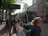 The tram is arriving at the tram stop Weesperplein where young women are waiting; free photo of Amsterdam city by Fons Heijnsbroek - street photography, Summer 2022